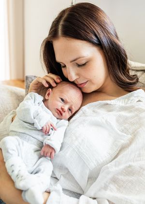 Mother tenderly holding newborn baby against her chest while gently touching infant's head.