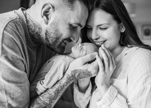 Black and white photo of tattooed father and mother lovingly gazing at their newborn baby.