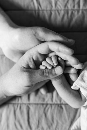 Black and white close-up of a newborn baby's tiny hand resting in a parent's gentle hands.