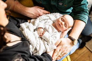 Parents tenderly cradle their sleeping newborn baby wrapped in a white knit blanket.