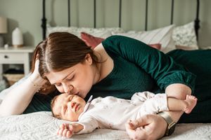 Mother in green dress lying on bed giving a gentle kiss to her newborn baby.