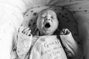 Adorable newborn baby yawning in a onesie reading Guess How Much I Love You.