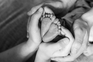 Black and white close-up of parents tenderly cupping their newborn baby's tiny feet.