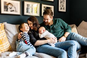 Happy family of four sitting on a couch smiling together with their newborn baby.