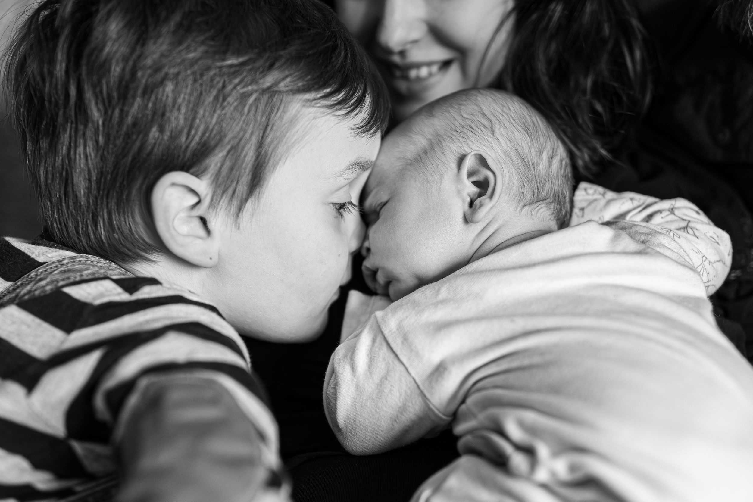 Black and white photo of a young child gently touching foreheads with a newborn sibling.