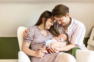 Loving parents sitting together in a white chair, tenderly holding their newborn baby.