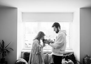 Black and white photo of a bearded father sharing a tender moment with his young daughter by a window.