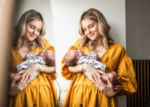 A mirror reflection of a smiling woman in a yellow dress cradling her newborn baby.