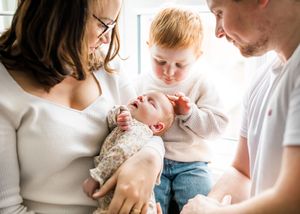 Close-up of parents and red-haired toddler lovingly looking at their newborn baby together.
