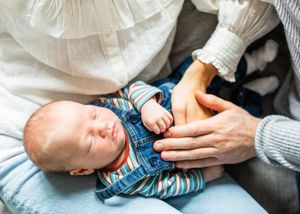 Sleeping newborn baby in striped outfit held in parents arms on light background.