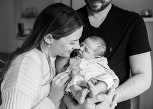 Black and white photo of new parents sharing a tender moment, gently kissing their newborn baby.