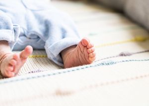 Close-up of tiny newborn baby feet in blue outfit resting on colorful patterned blanket.