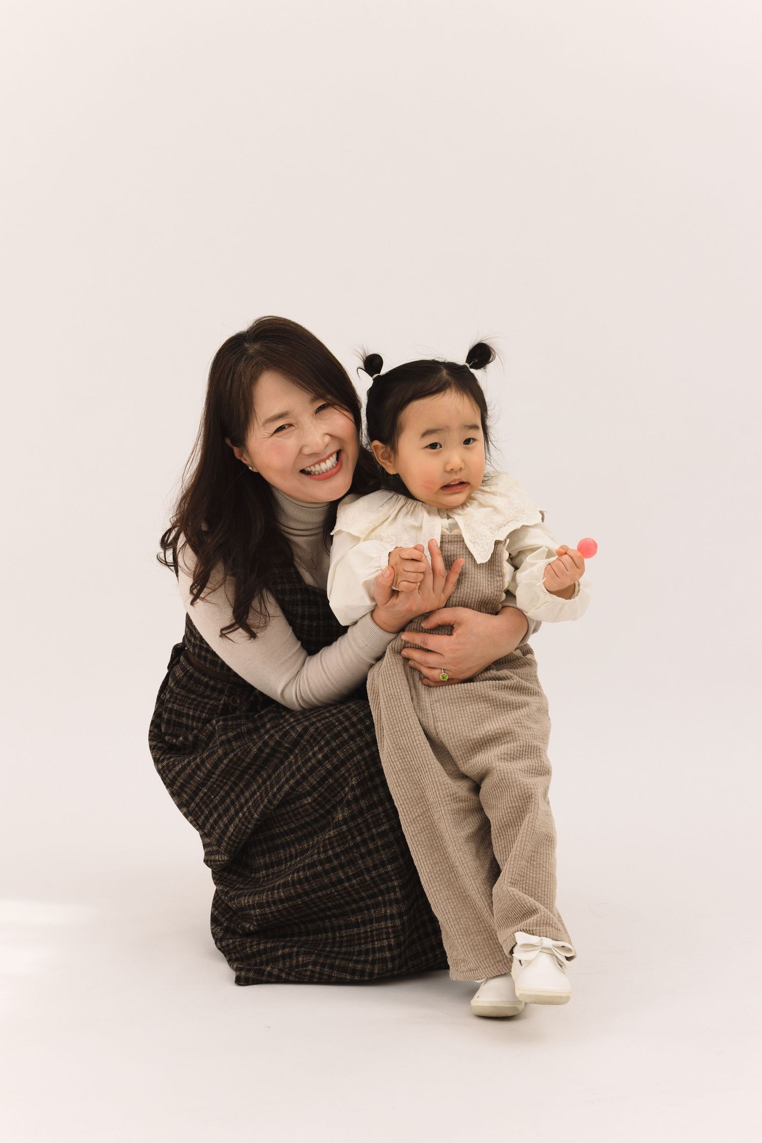 A parent and child share playful moments together while sitting on a white studio floor.