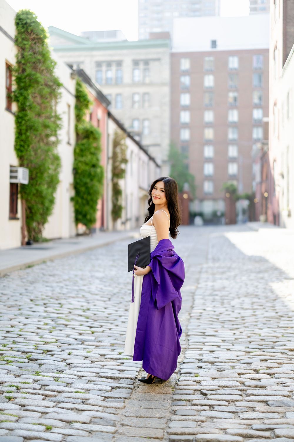 A person in a flowing purple dress twirls on a cobblestone street near historic brick buildings.