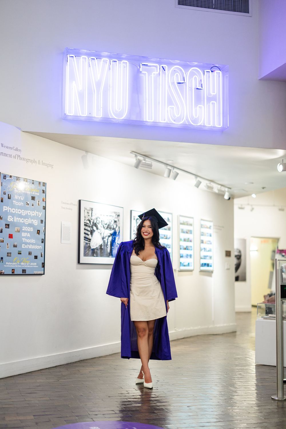 Art gallery interior with white walls, neon signage, and graduation cap-wearing figure in blue academic regalia.