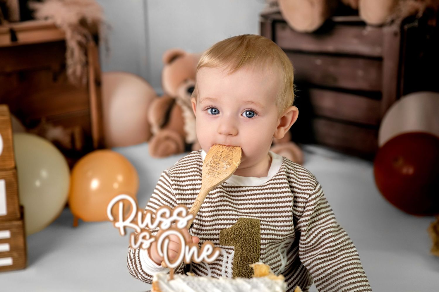 Baby wearing black and white striped shirt sits at table with birthday decorations and orange balloons.