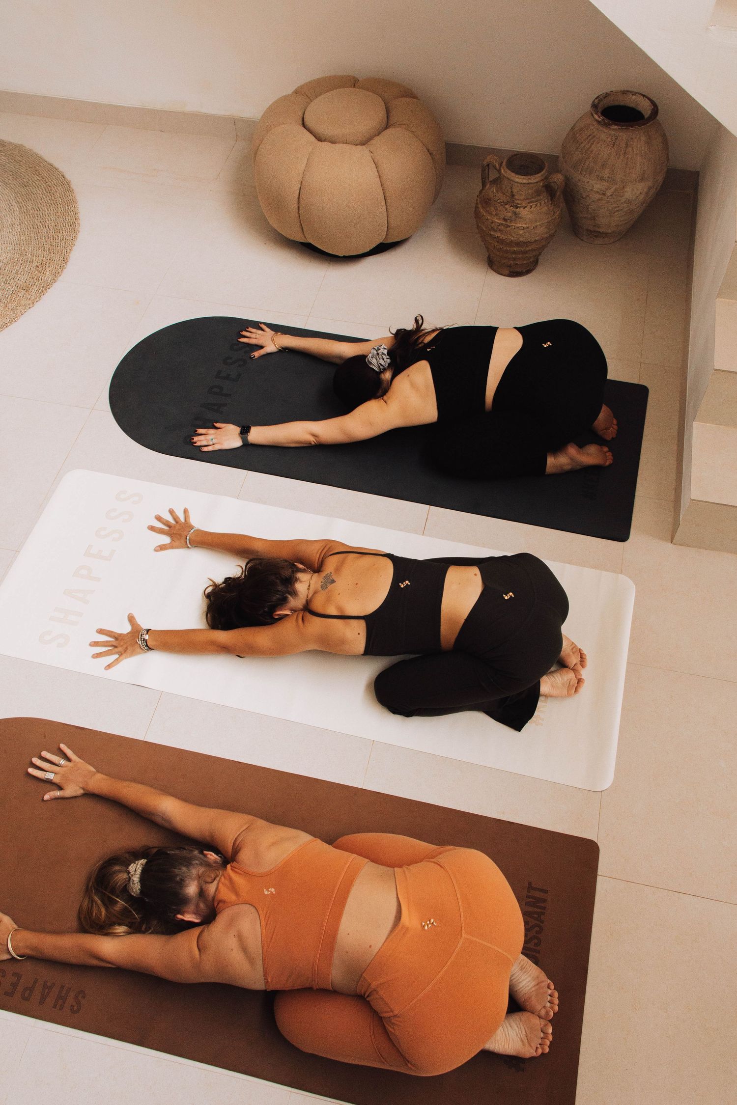 Three women practice child's pose on yoga mats in a serene, minimalist studio with earthy decor.