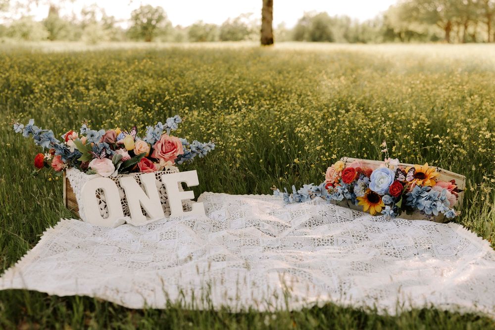 Vintage-inspired picnic setup with white lace blanket and decorative elements in a sunlit meadow field.