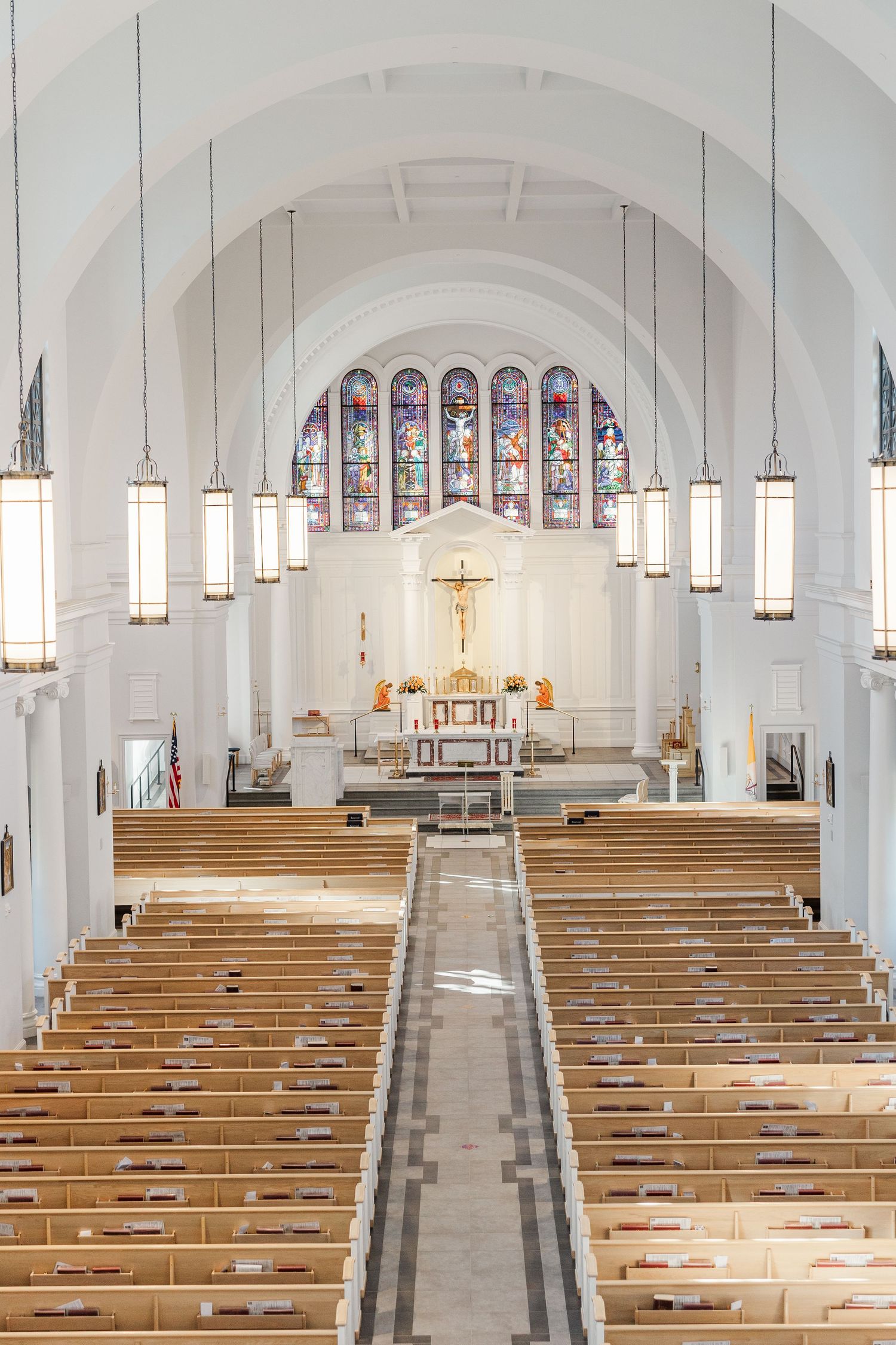 Interior view of a bright white church sanctuary with wooden pews and stained glass windows under arched ceilings.
