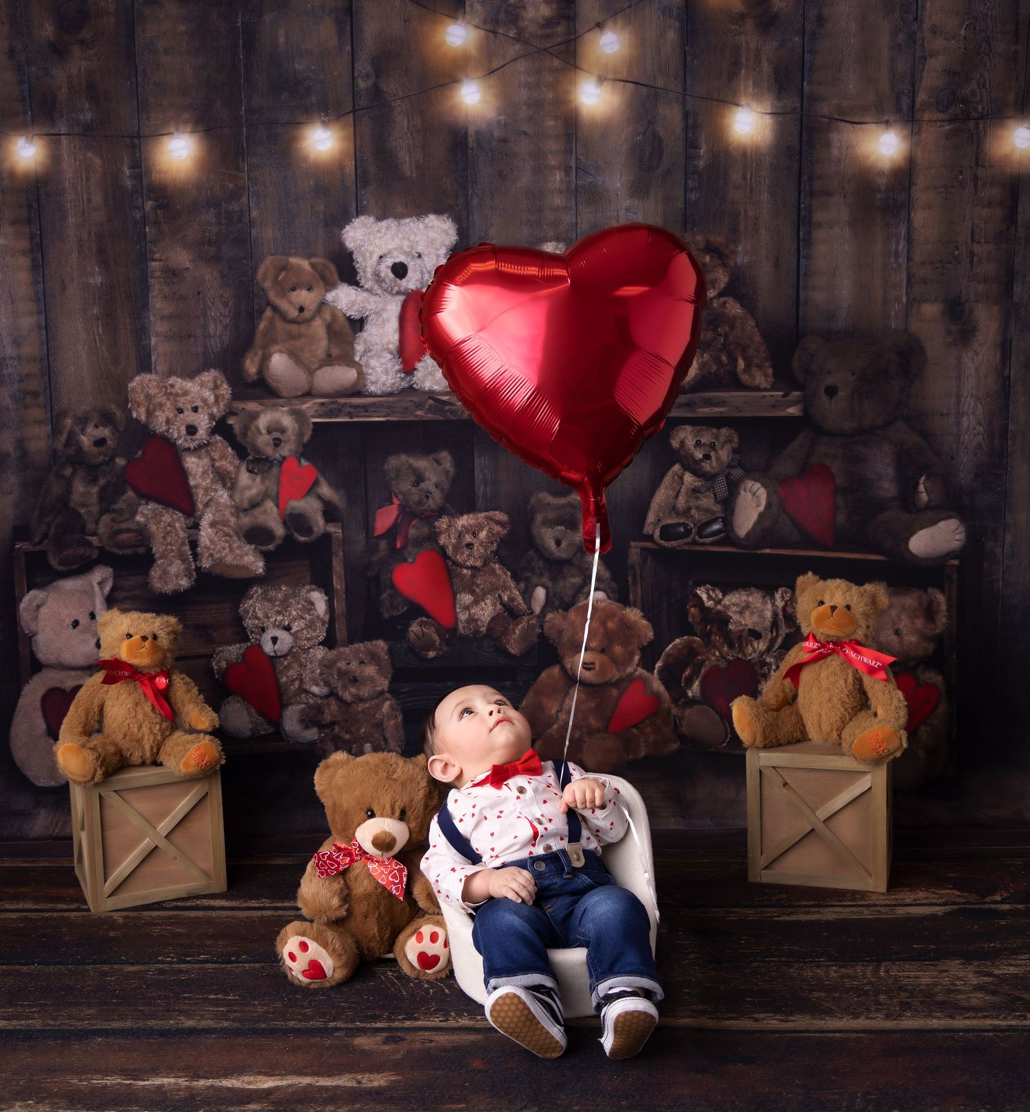 A romantic Valentine's Day photo setup with teddy bears, string lights, and a red heart balloon against a rustic wood backdrop.