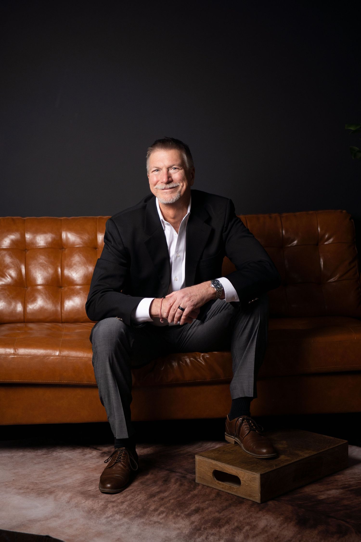Professional studio portraits of someone wearing a navy blazer, red top and white sneakers while sitting on a wooden chair.