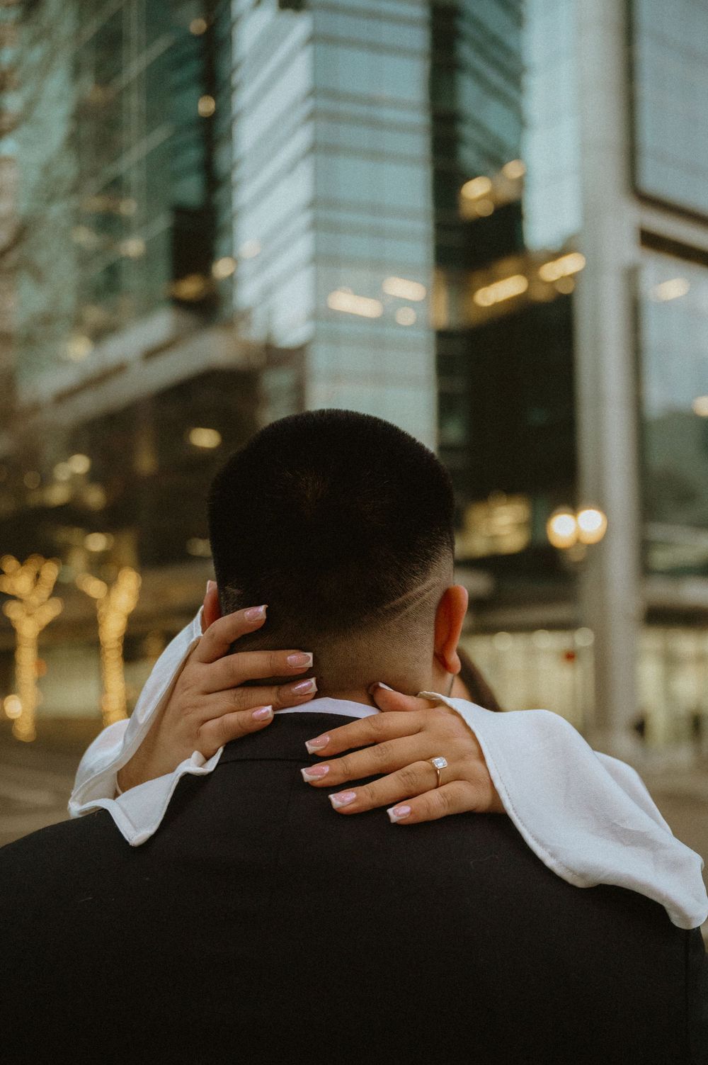 Close-up shot showing hands gently caressing in an intimate moment against urban backdrop.