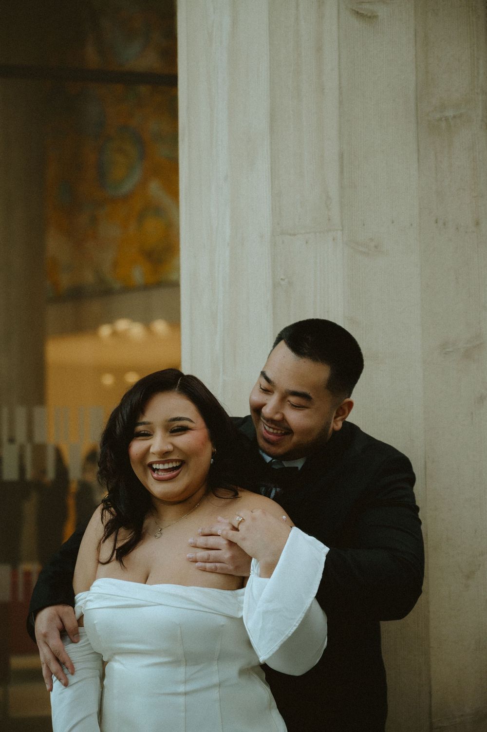 Happy couple in formal attire sharing intimate moments and laughter between architectural columns.