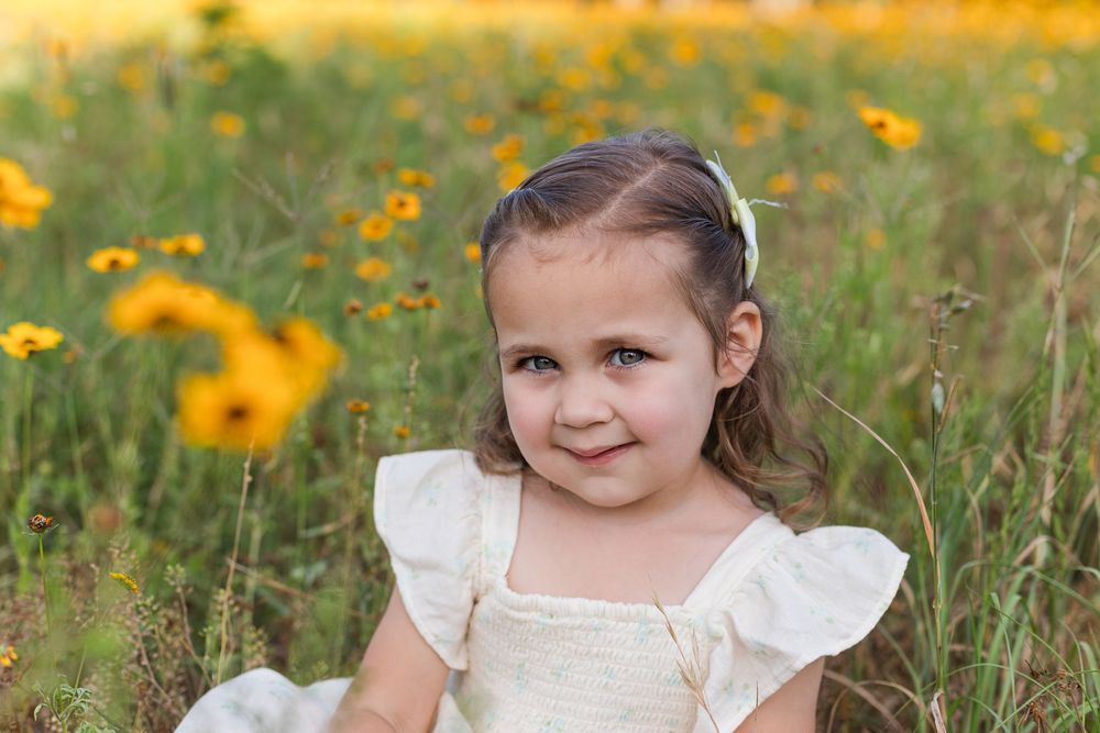 Children in white dresses pose in a vibrant field of yellow wildflowers on a sunny day.