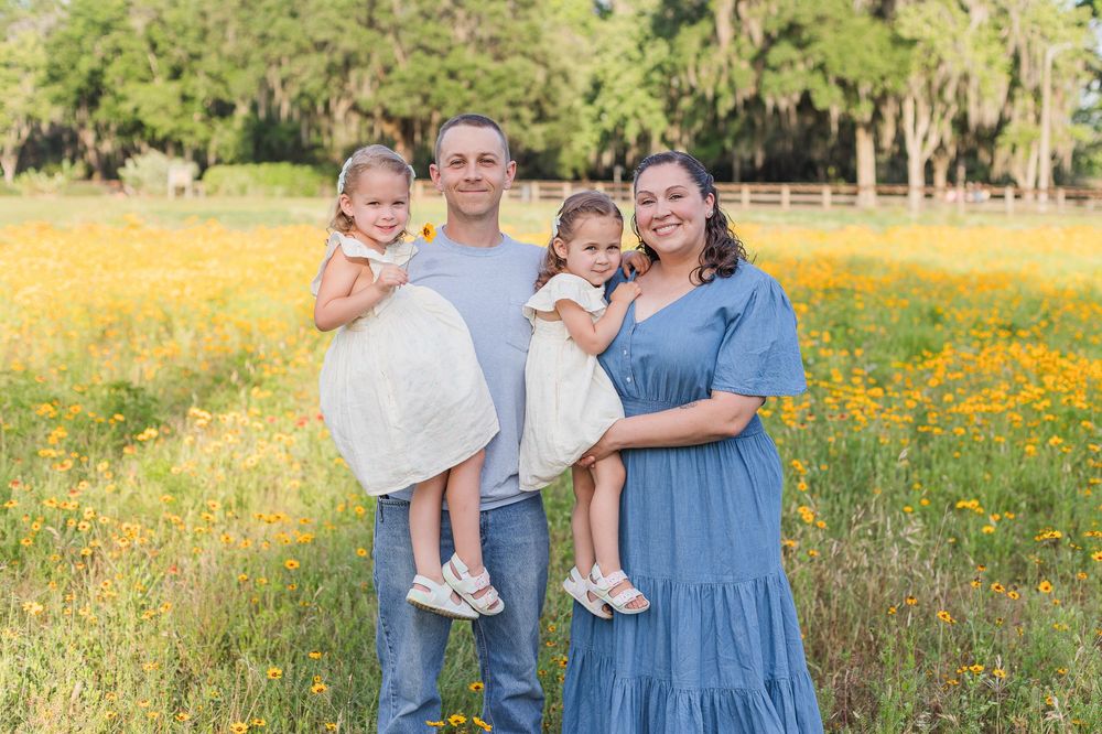 A family poses together in a field of yellow wildflowers with palm trees in the background.