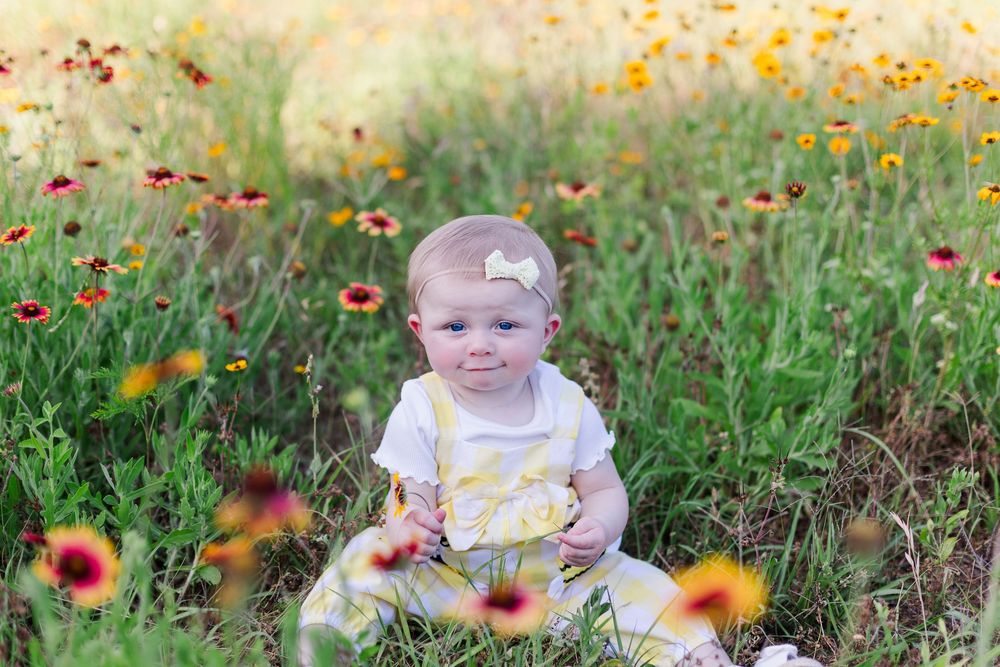 A child sits in a grassy meadow surrounded by vibrant orange and yellow wildflowers on a sunny day.