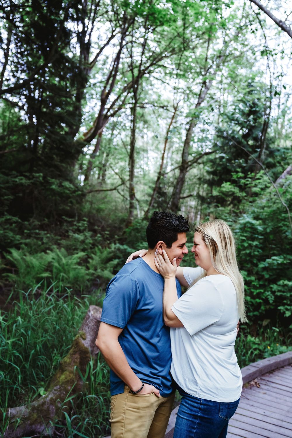 A couple shares an intimate moment on a wooden boardwalk surrounded by greenery.