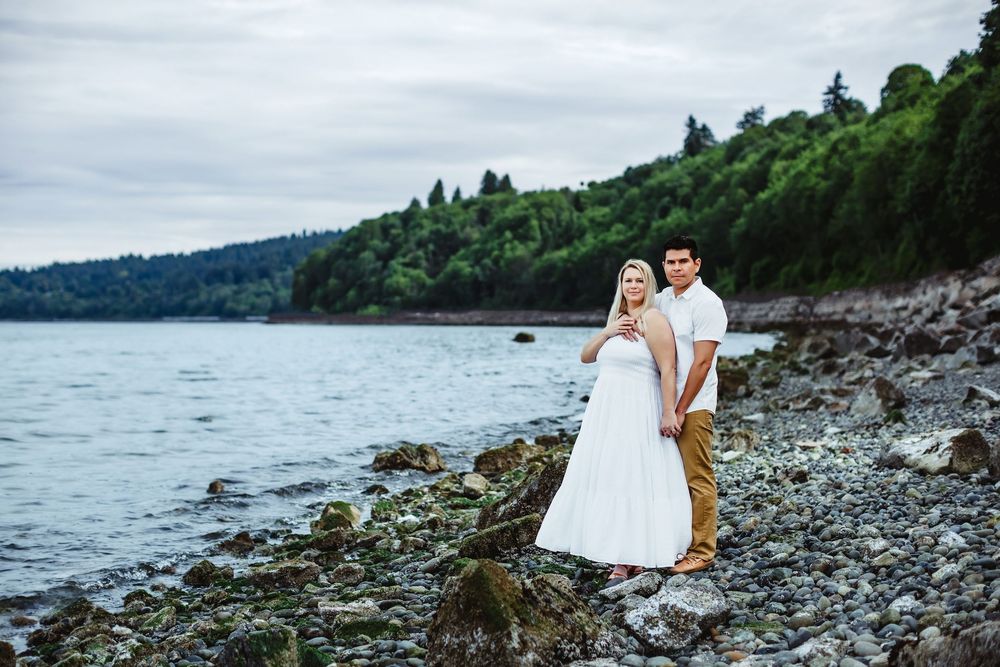 A couple walks along a rocky beach shoreline on an overcast day.