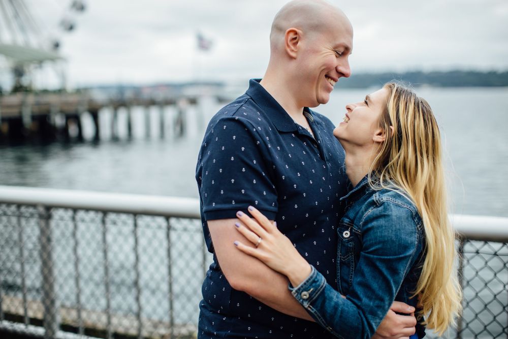 Romantic couple shares intimate moments along a waterfront railing during an outdoor photoshoot.