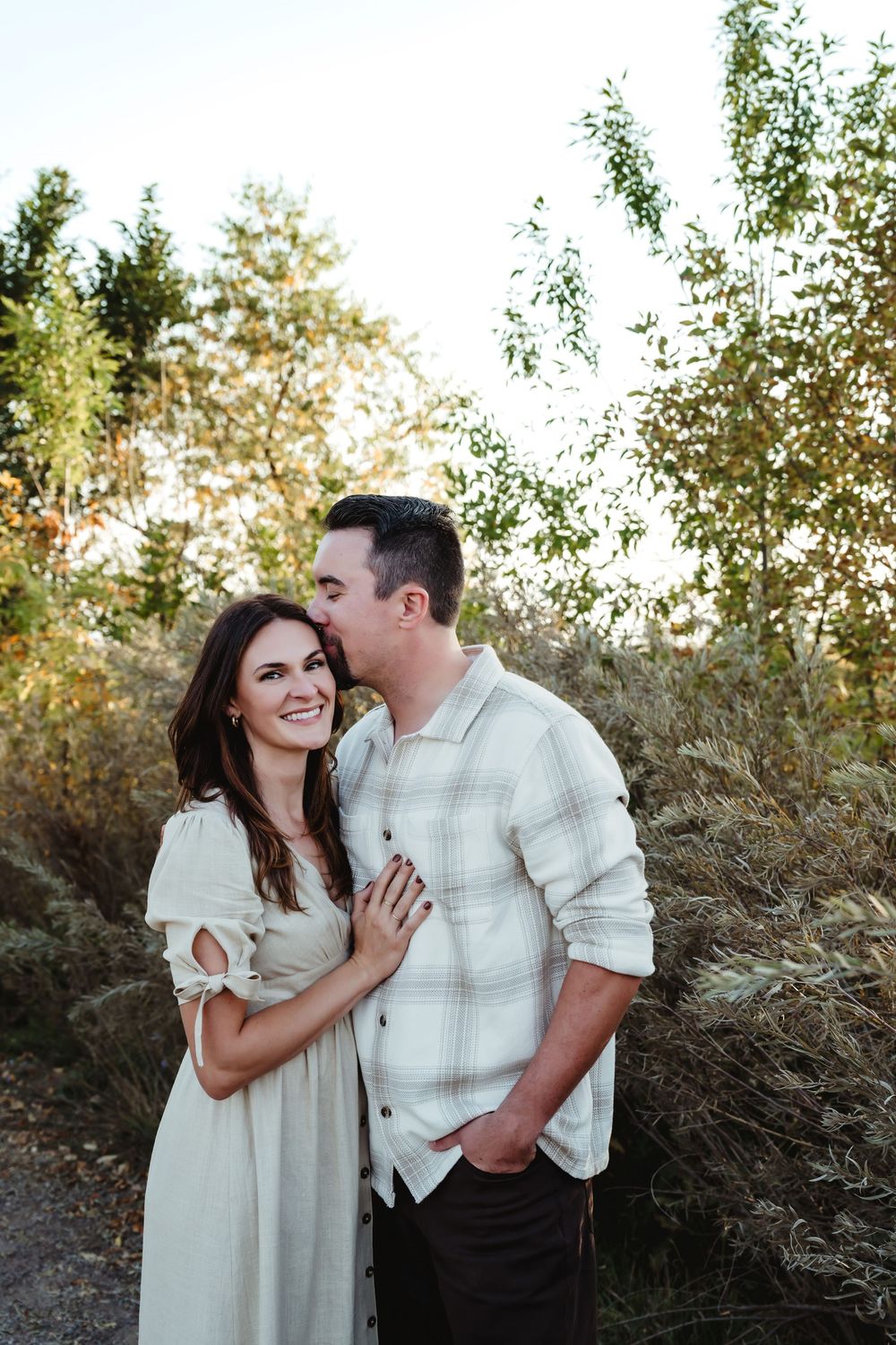 Couple shares tender moments against natural desert brush backdrop during sunset.