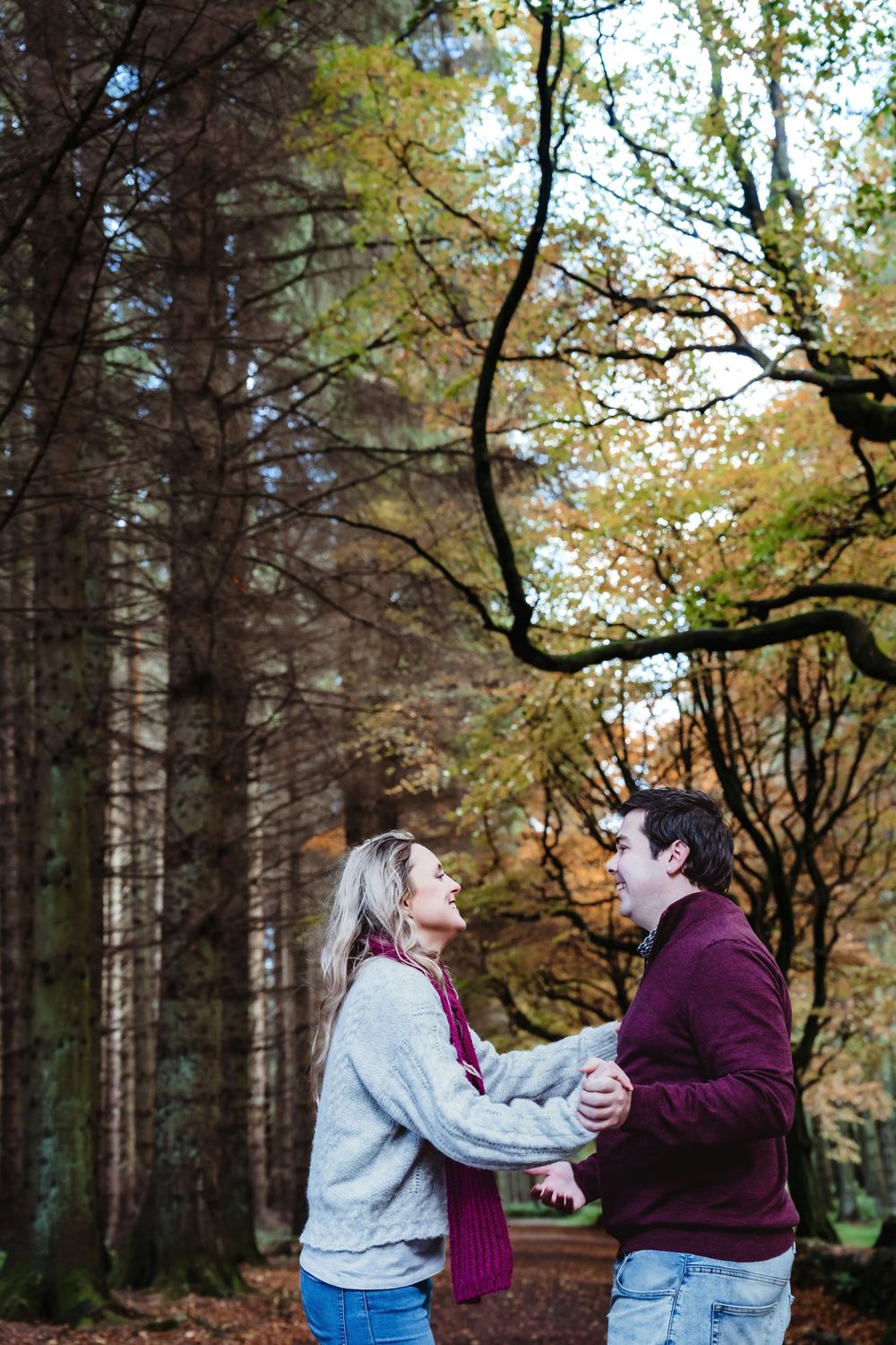 A couple shares a joyful moment in an autumn forest setting.