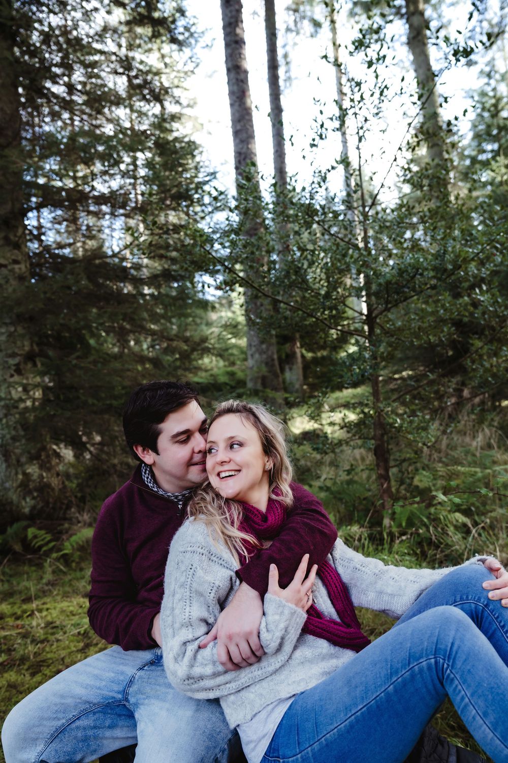 A romantic couple embraces while relaxing in a wooded forest setting.