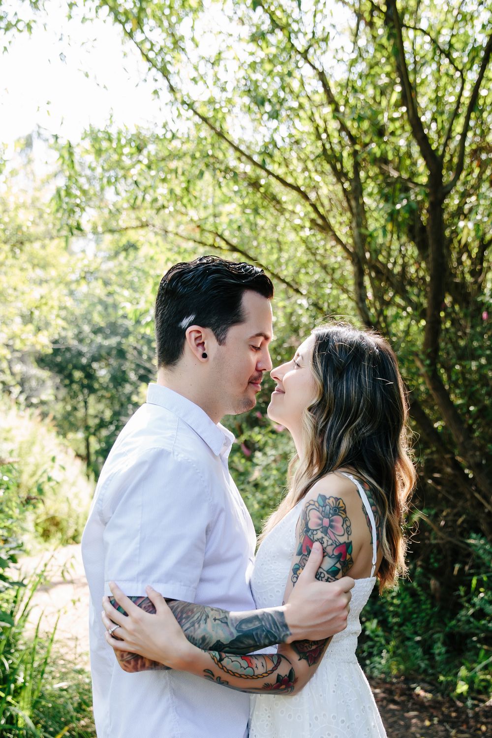 Couple shares romantic moments in sunlit garden setting with tattoo details visible.