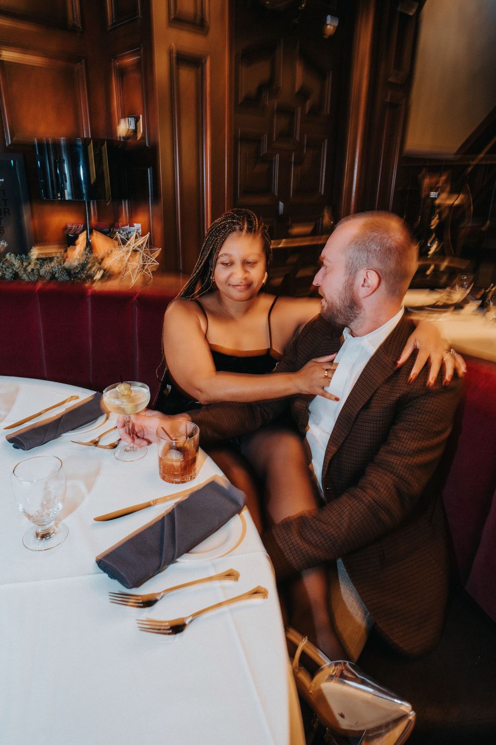 A couple shares an intimate moment at an upscale restaurant with warm lighting and elegant table settings.