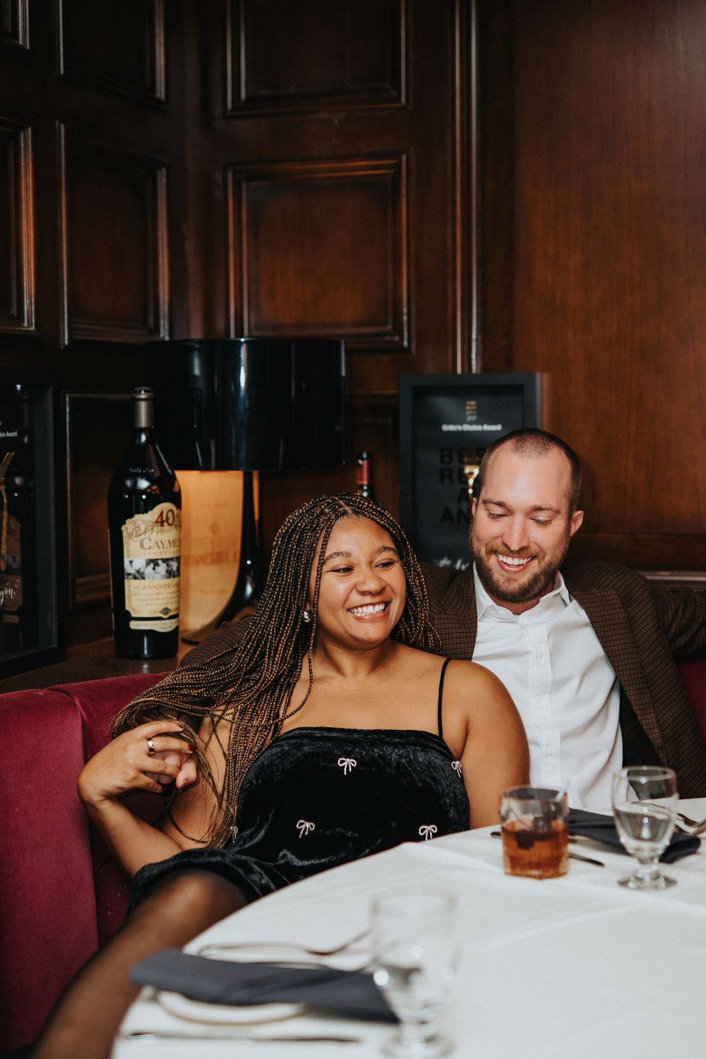 A couple enjoys drinks and conversation at an upscale restaurant with wood-paneled walls.
