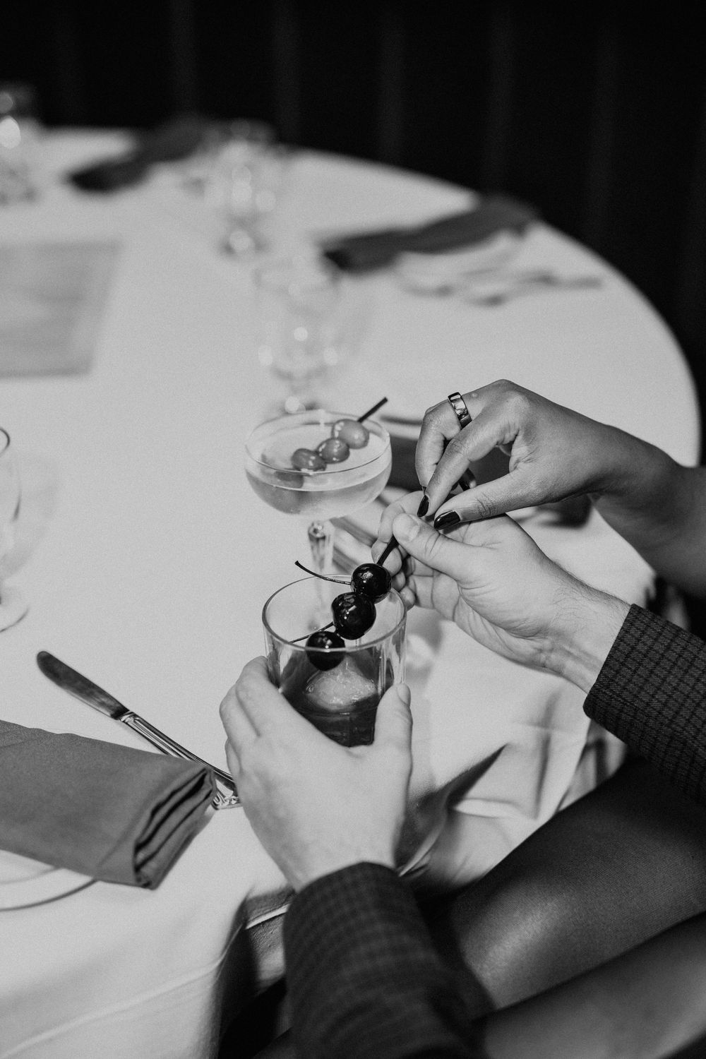 Hands preparing drinks at a white tablecloth setting in black and white photography.
