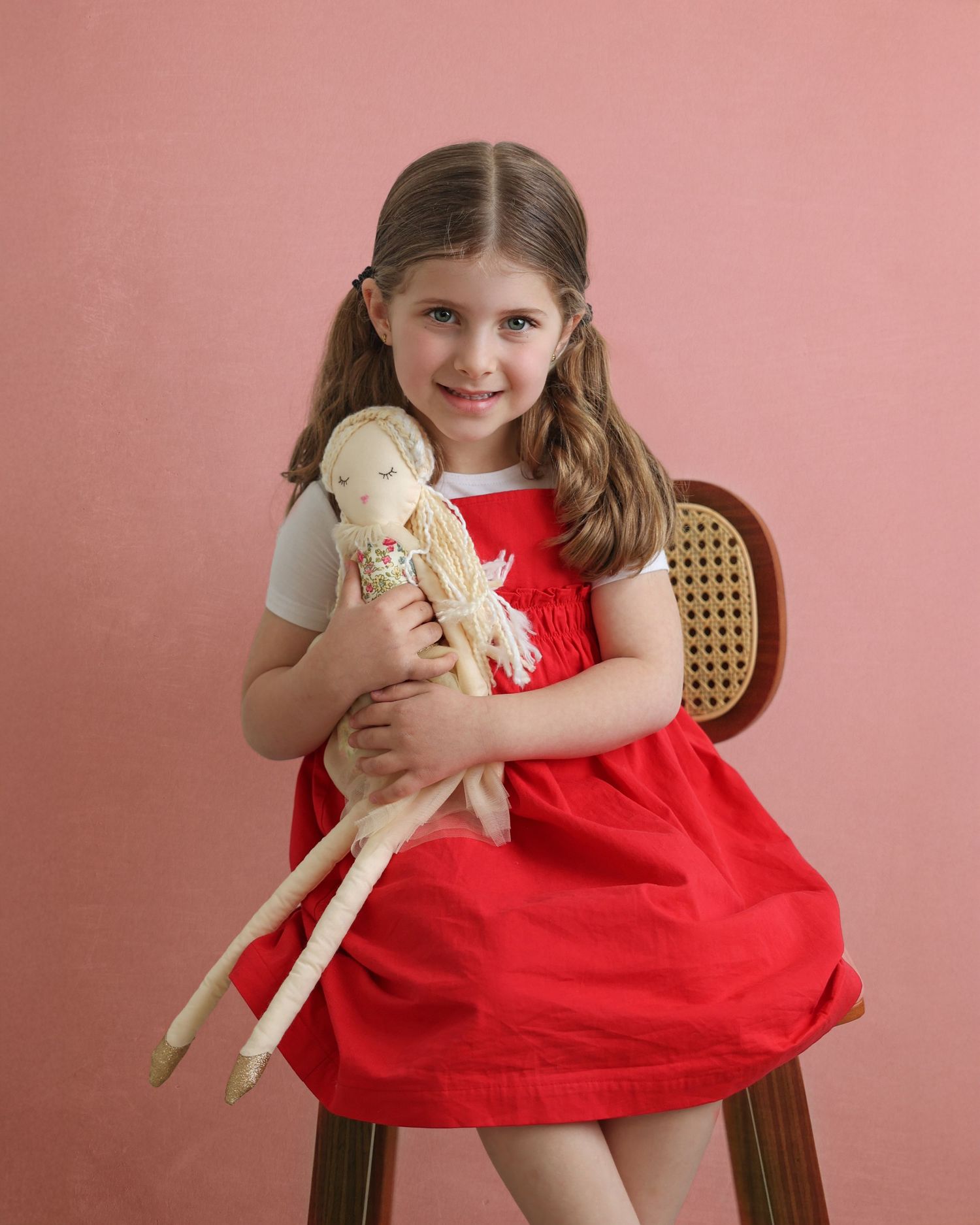 studio image of a little girl with pigtails hugging her pretty doll