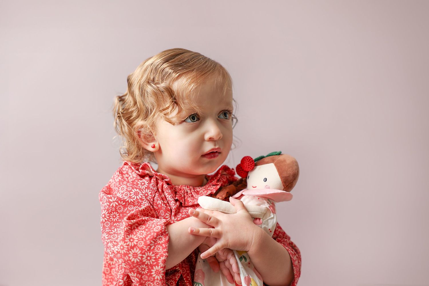 toddler girl with a serious expression hugging her doll