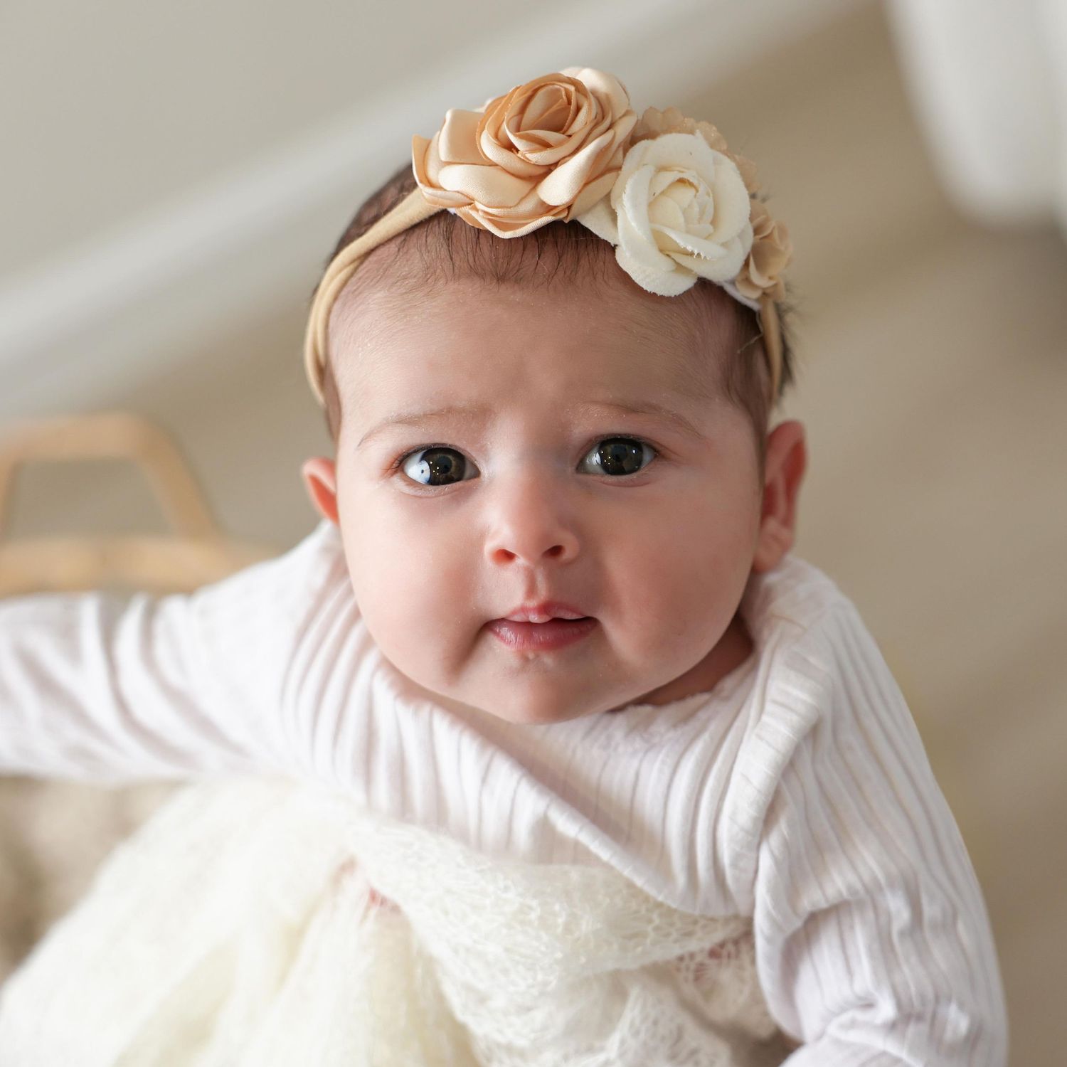 Close up portrait of infant girl gazing wide-eyed at the camera wearing a floral headband
