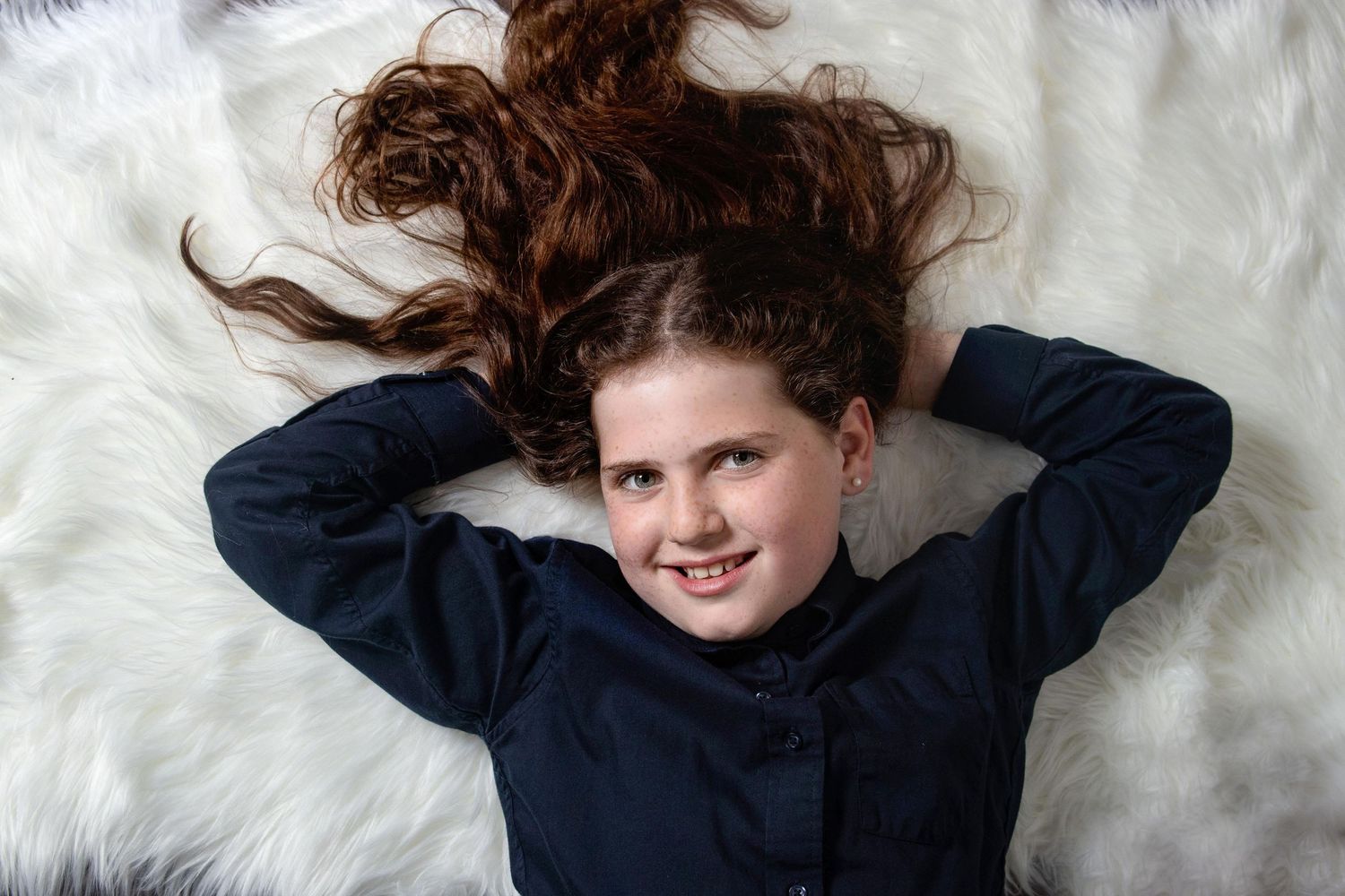 Overhead studio portrait of girl lying on a white fur rug with her long hair fanned out around hierhead