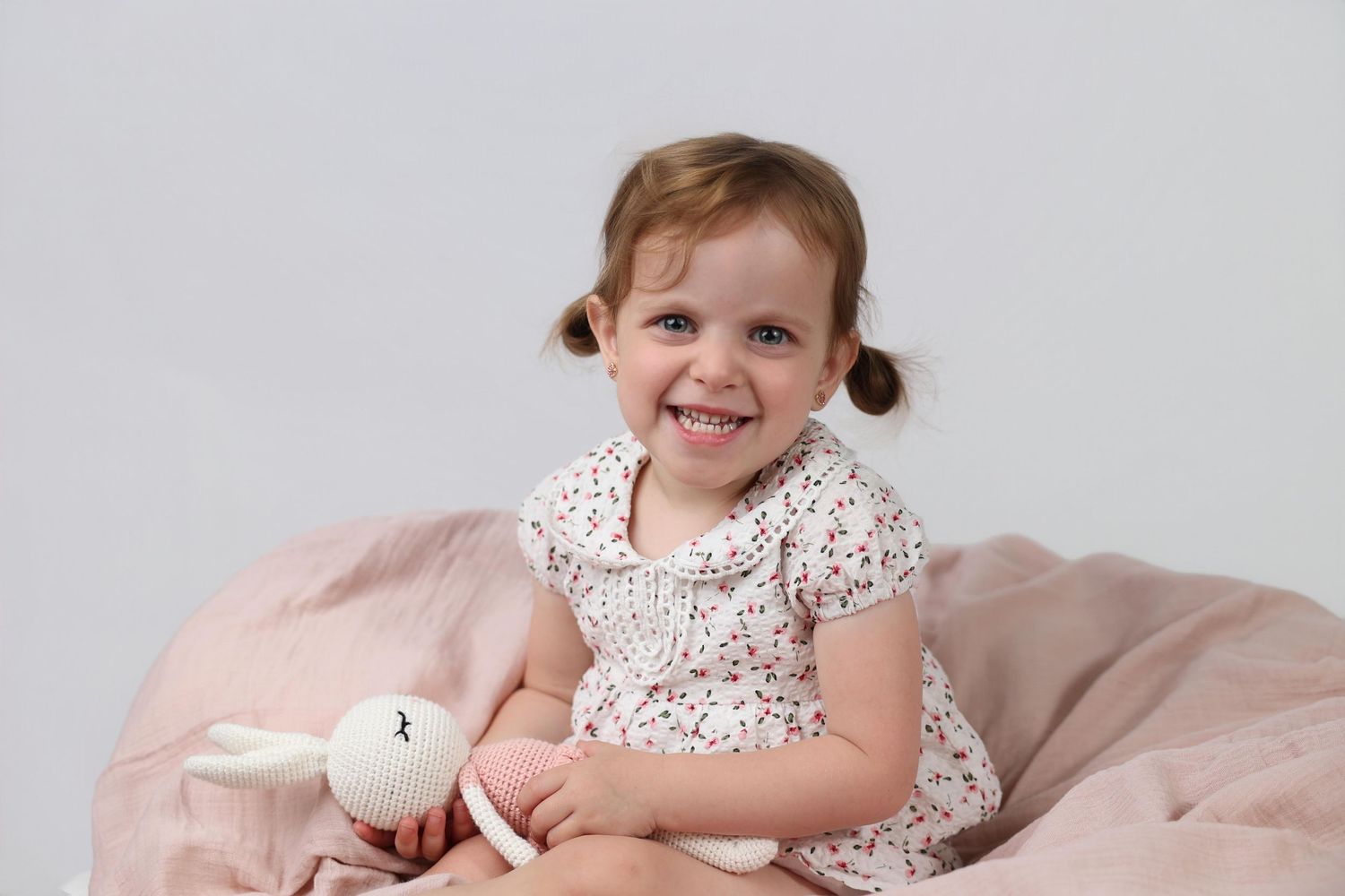 indoor portrait of little girl sitting on a muslin blanket holding a knit doll
