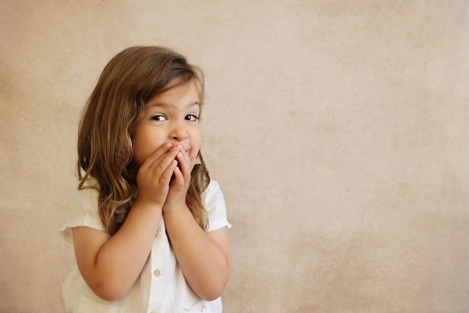 Candid studio portrait of a 3-year-old upsherin boy with long hair giggling and covering his mouth