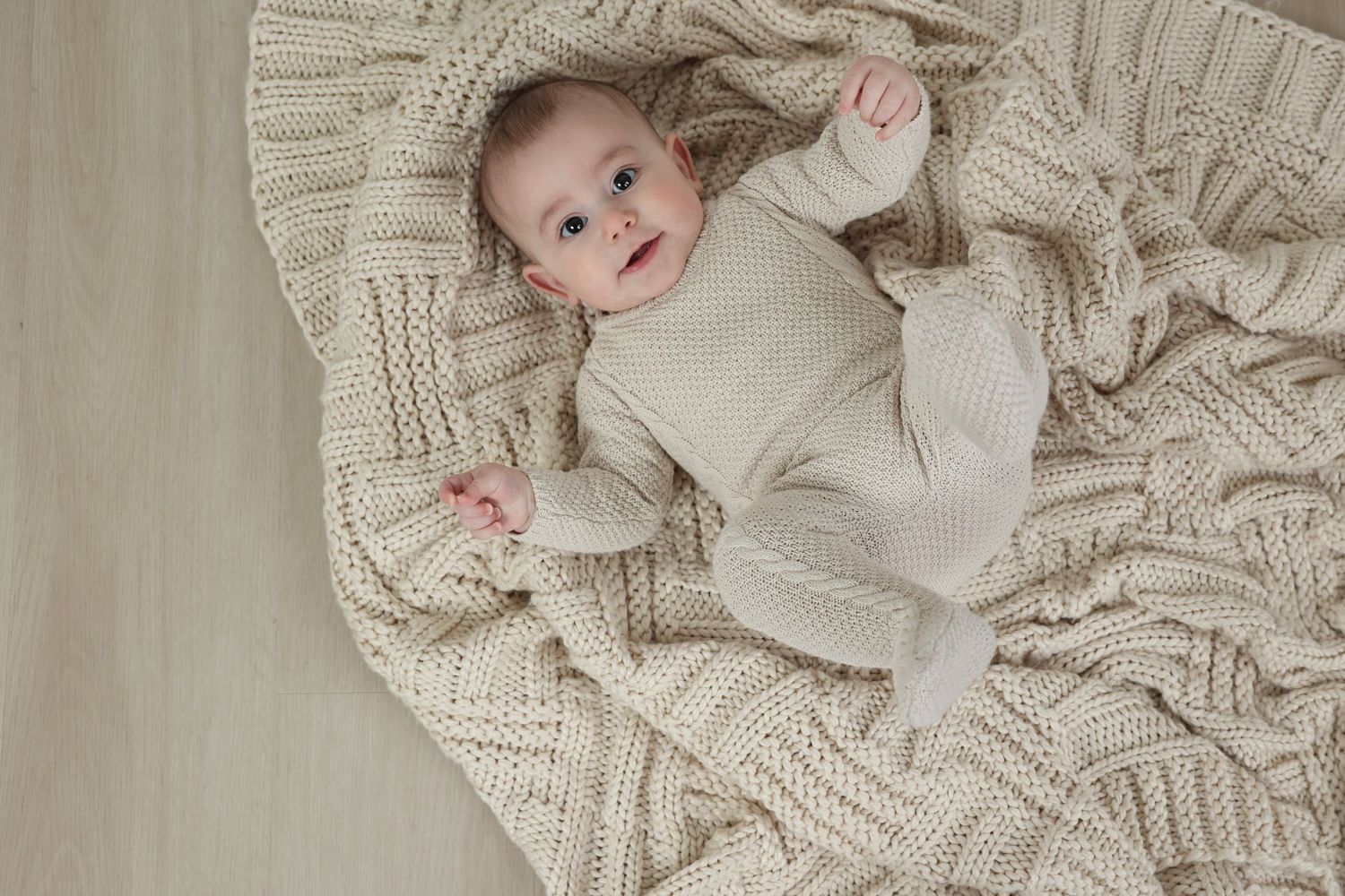 Overhead milestone studio photo of an infant boy lying comfortably on his back and making eye contact with the camera