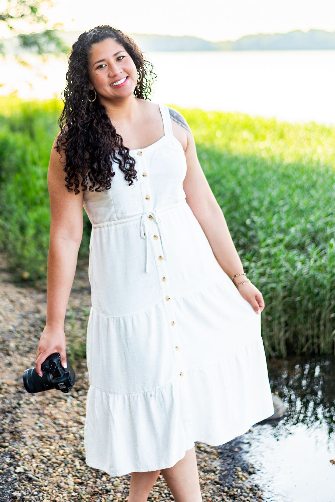 Woman in white sleeveless dress poses outdoors near water during golden hour photoshoot. RVA Photographer affordable near you