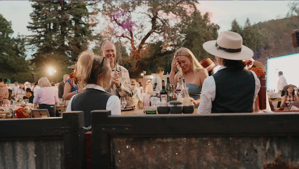 Outdoor wedding ceremony and reception scenes at sunset with guests mingling and celebrating under string lights.