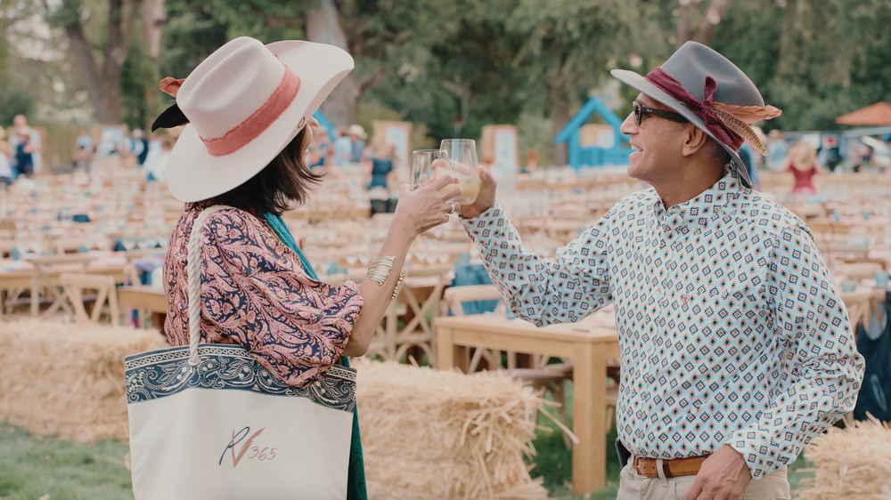 A couple in casual attire shares a romantic moment while sitting together at an outdoor restaurant table.